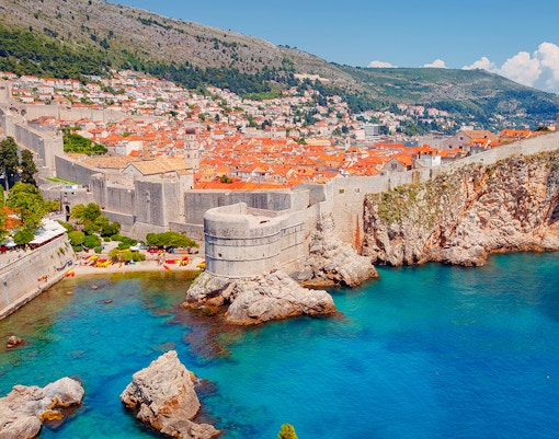 Dubrovnik city walls overlooking the Adriatic Sea with historic buildings and rocky coastline.