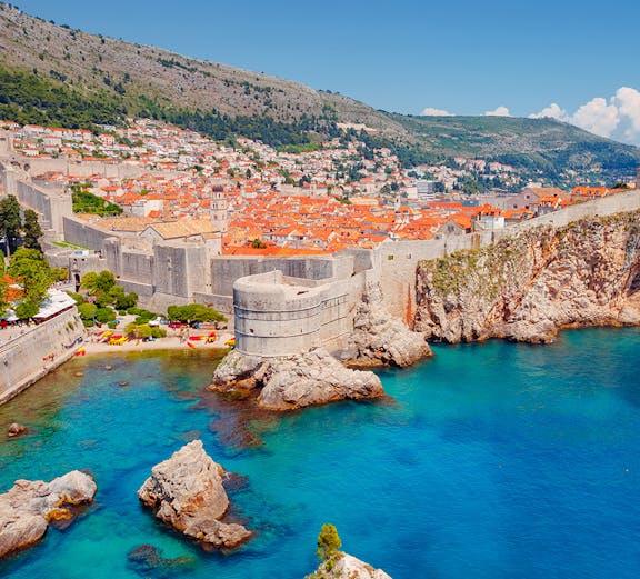 Dubrovnik city walls overlooking the Adriatic Sea with historic buildings and rocky coastline.