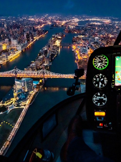 Helicopter view of NYC skyline and Queensboro Bridge at night.