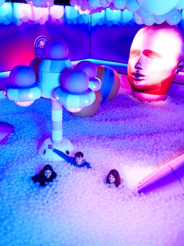 Visitors enjoying Bubble Planet installation with colorful lights and giant head sculpture.