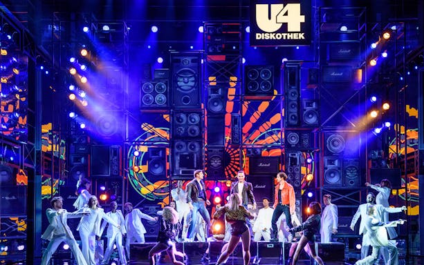 Performers on stage at Ronacher for "Rock Me Amadeus – The Falco Musical" with vibrant lights and speakers.
