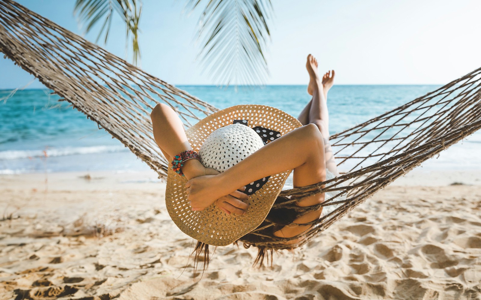Woman relaxing in a hammock on a sandy beach with ocean view.