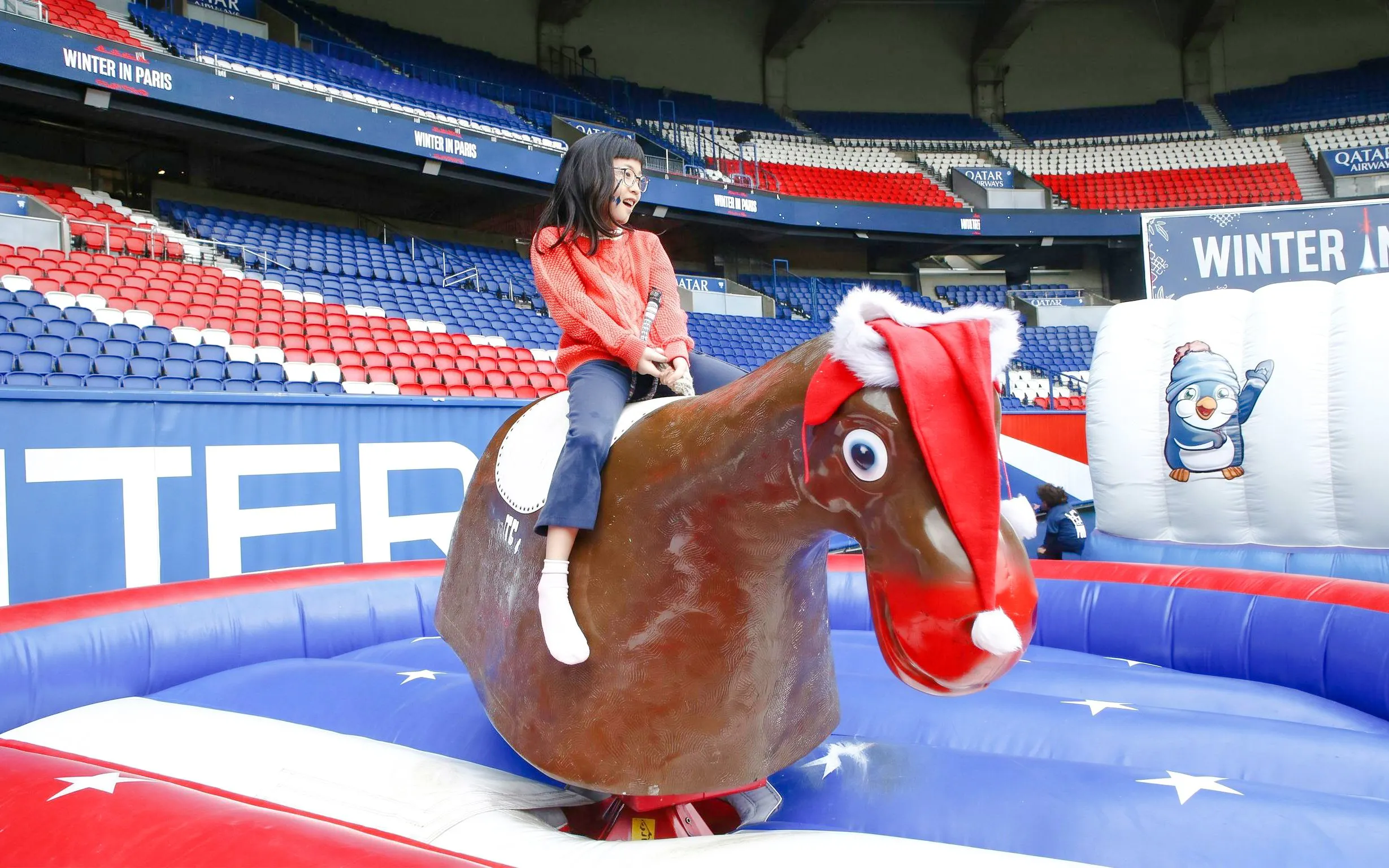 Child riding a mechanical reindeer at PSG stadium during Christmas tour in Paris.