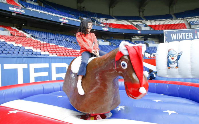 Child riding a mechanical reindeer at PSG stadium during Christmas tour in Paris.