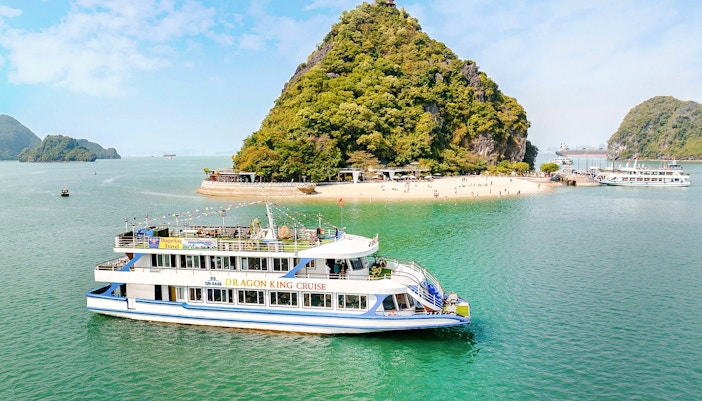 Cruise ship "DRAGON KING CRUISE" sailing in Ha Long Bay near a beach.