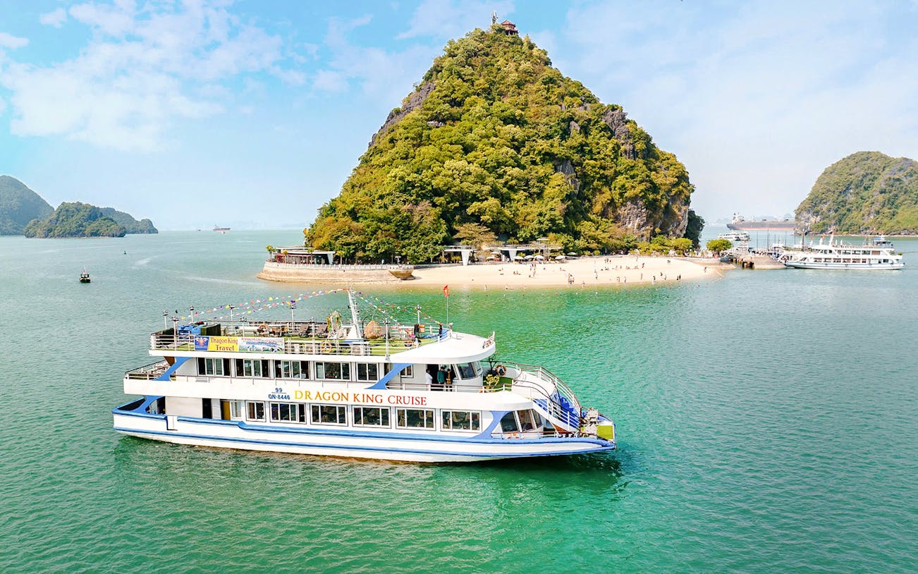 Cruise ship "DRAGON KING CRUISE" sailing in Ha Long Bay near a beach.