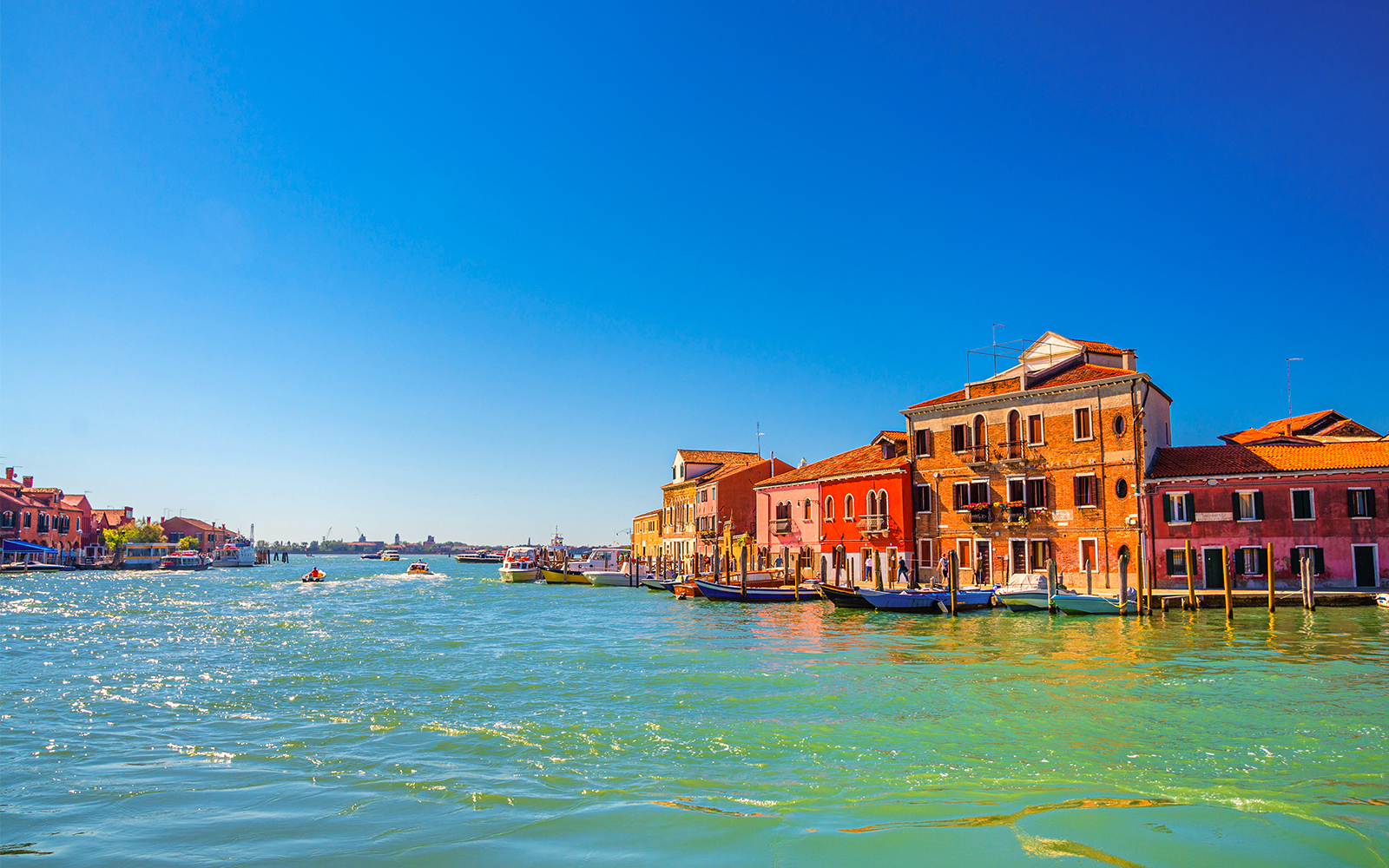 Murano canal with boats and colorful buildings in Venetian Lagoon.