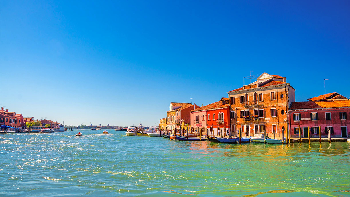 Murano canal with boats and colorful buildings in Venetian Lagoon.