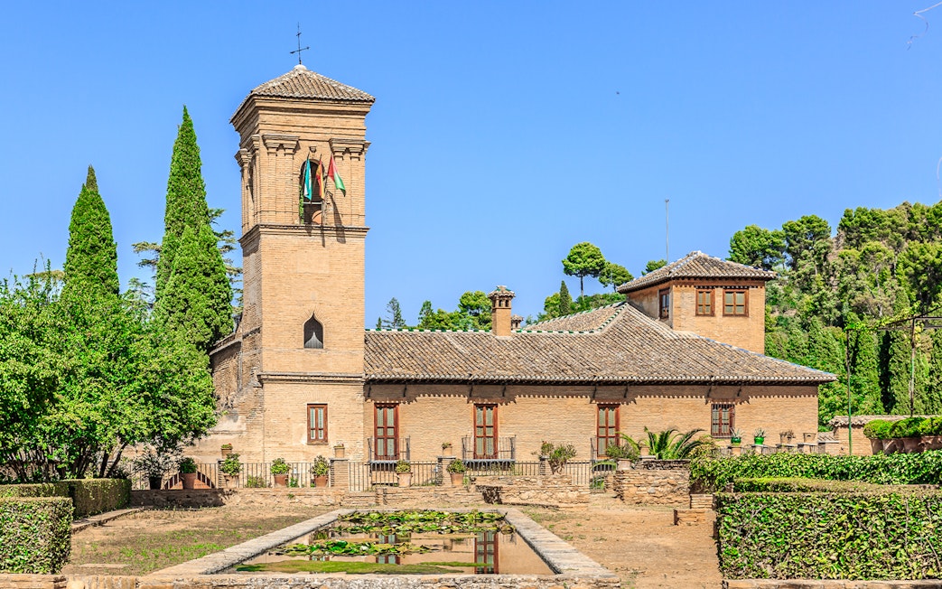 Alhambra tower and gardens with lush greenery under a clear blue sky.