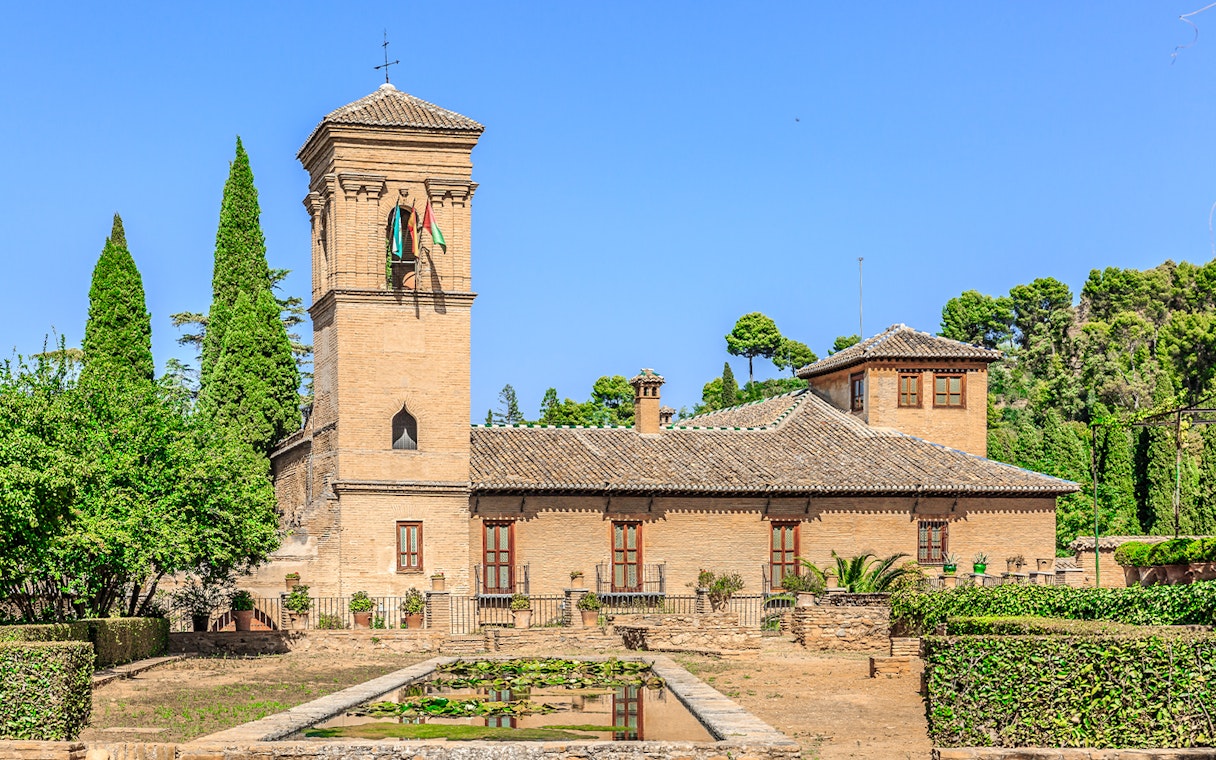 Alhambra tower and gardens with lush greenery under a clear blue sky.