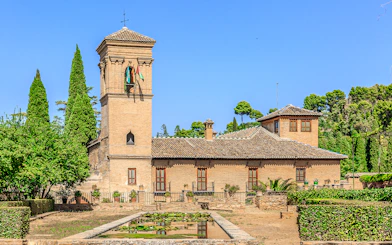 Alhambra tower and gardens with lush greenery under a clear blue sky.