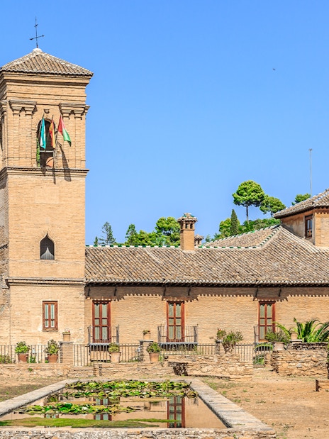 Alhambra tower and gardens with lush greenery under a clear blue sky.