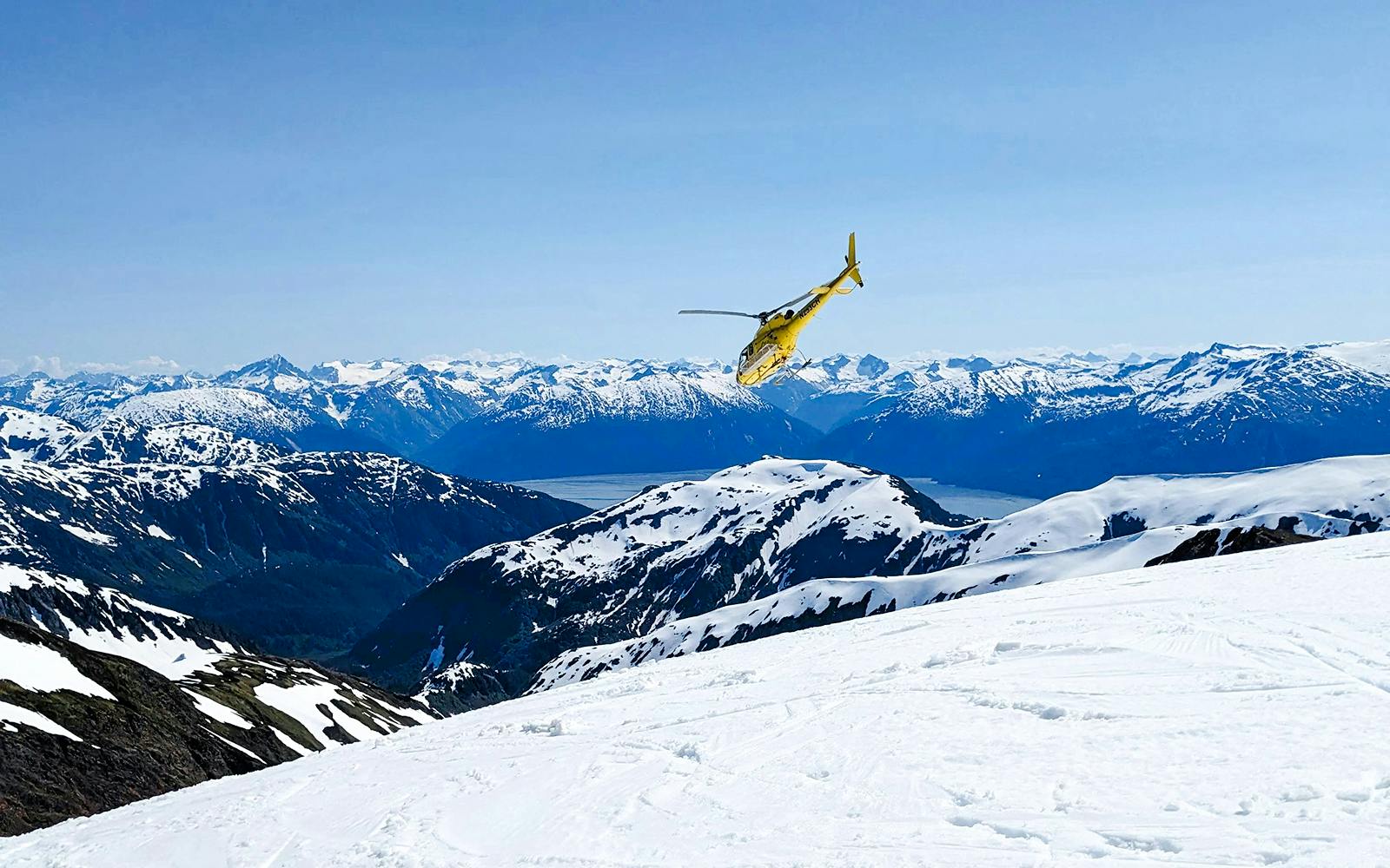 Helicopter flying over snowy mountains in Juneau during glacier landing tour.