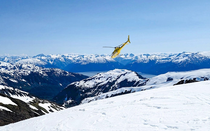 Helicopter flying over snowy mountains in Juneau during glacier landing tour.