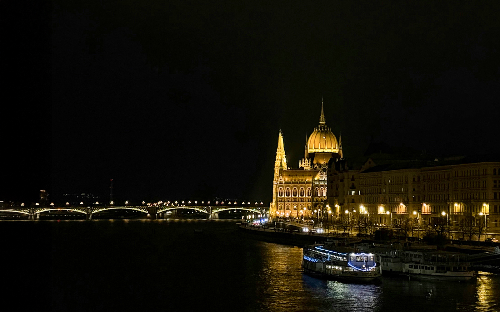 Night view of illuminated Parliament building and boat on Danube River, Budapest.