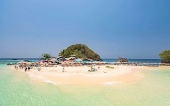 Phuket tour: tourists on Khai Island beach with colorful umbrellas and clear water.