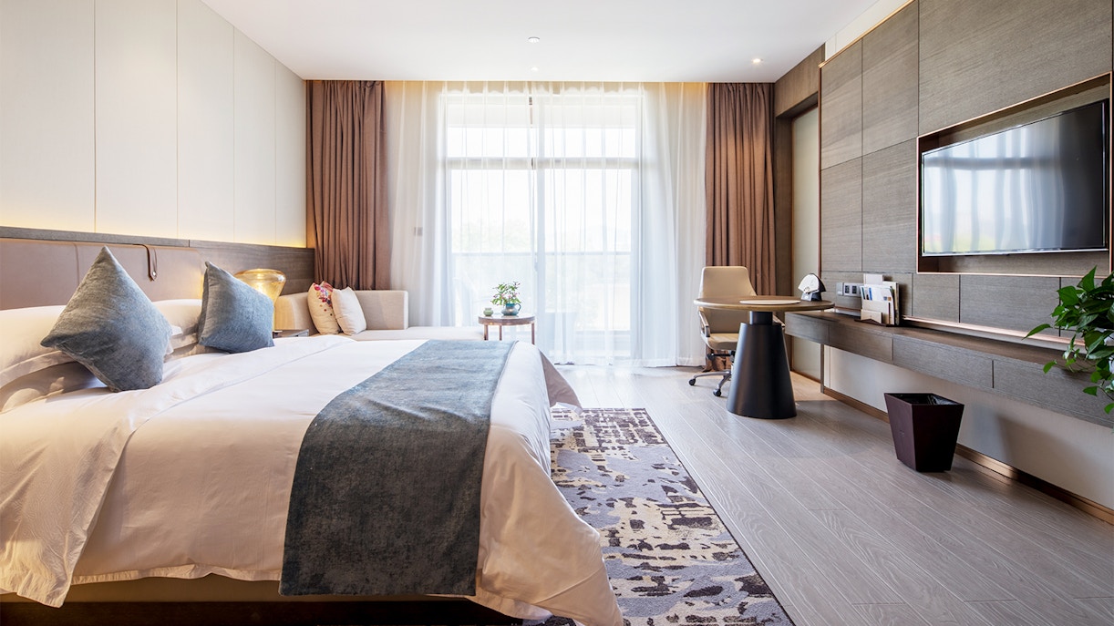 Luxury hotel room with king-size bed, modern decor, and large window.