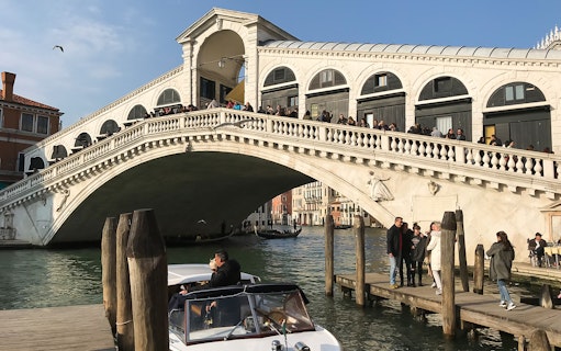 Rialto Bridge over Grand Canal in Venice with tourists and boat.