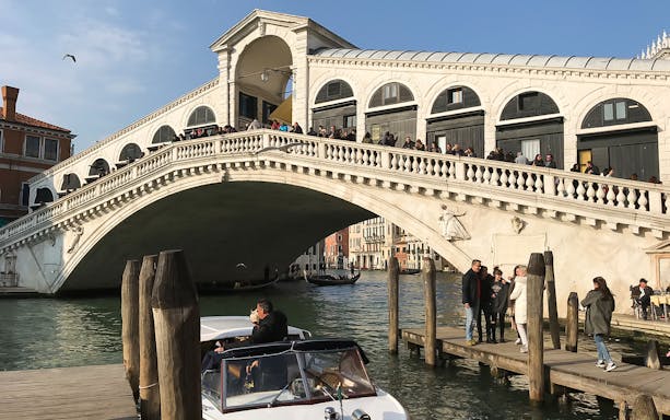Rialto Bridge over Grand Canal in Venice with tourists and boat.