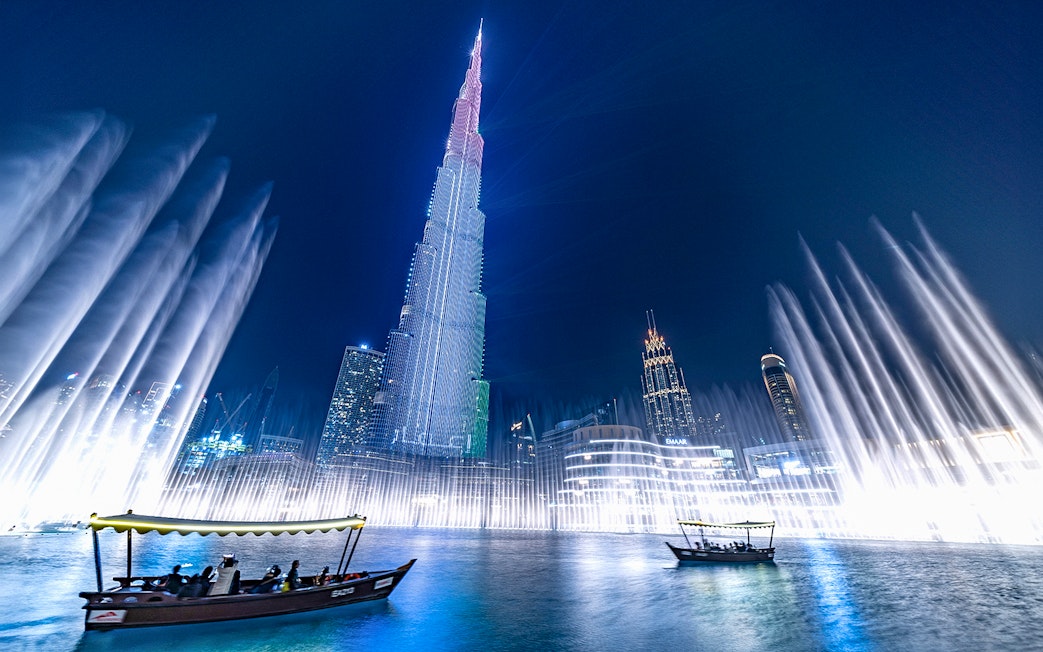 Dubai Fountain show with traditional abra boat on Burj Khalifa Lake at night.