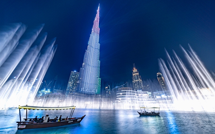Dubai Fountain show with traditional abra boat on Burj Khalifa Lake at night.
