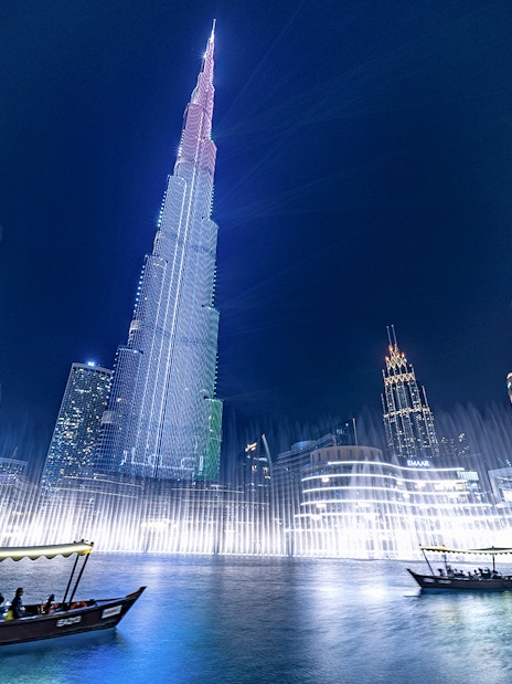 Dubai Fountain show with traditional abra boat on Burj Khalifa Lake at night.