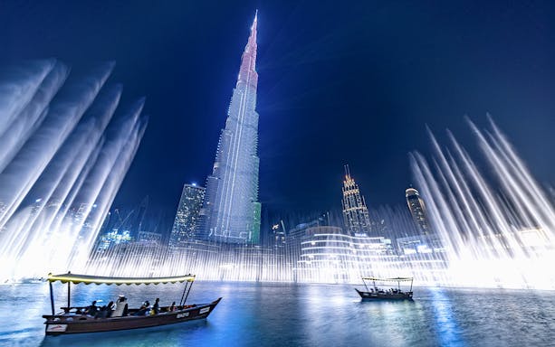 Dubai Fountain show with traditional abra boat on Burj Khalifa Lake at night.