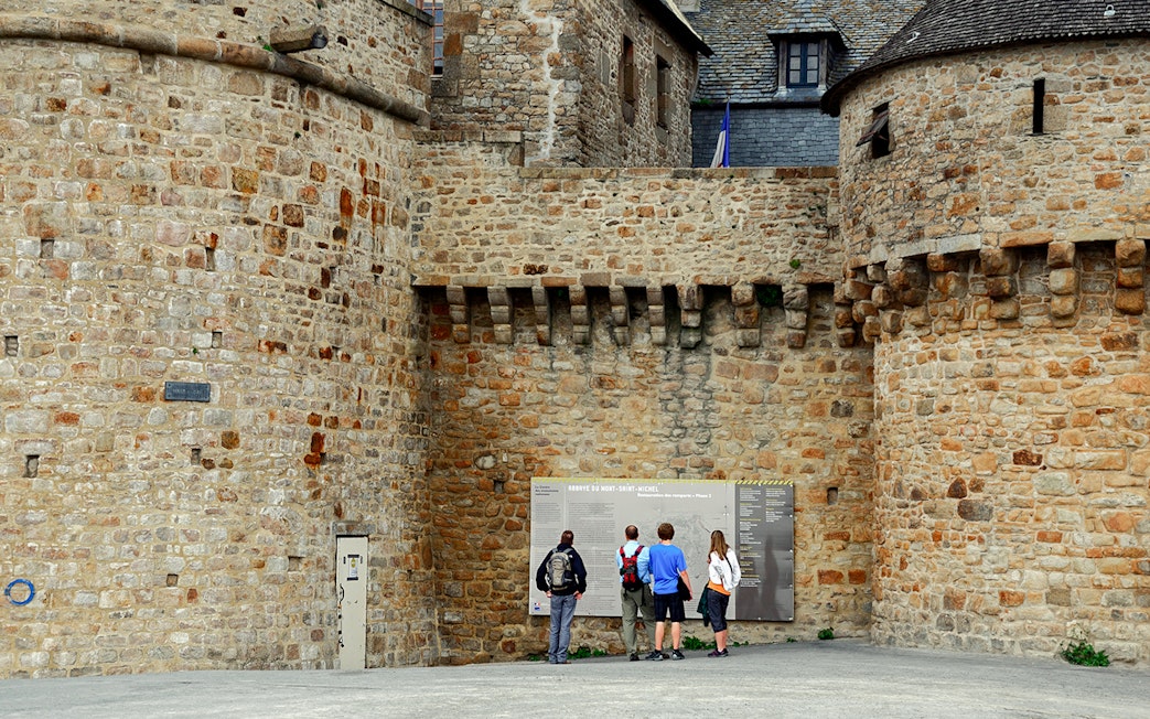 Visitors reading information on Mont Saint Michel's historic stone walls.