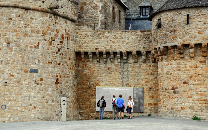Visitors reading information on Mont Saint Michel's historic stone walls.
