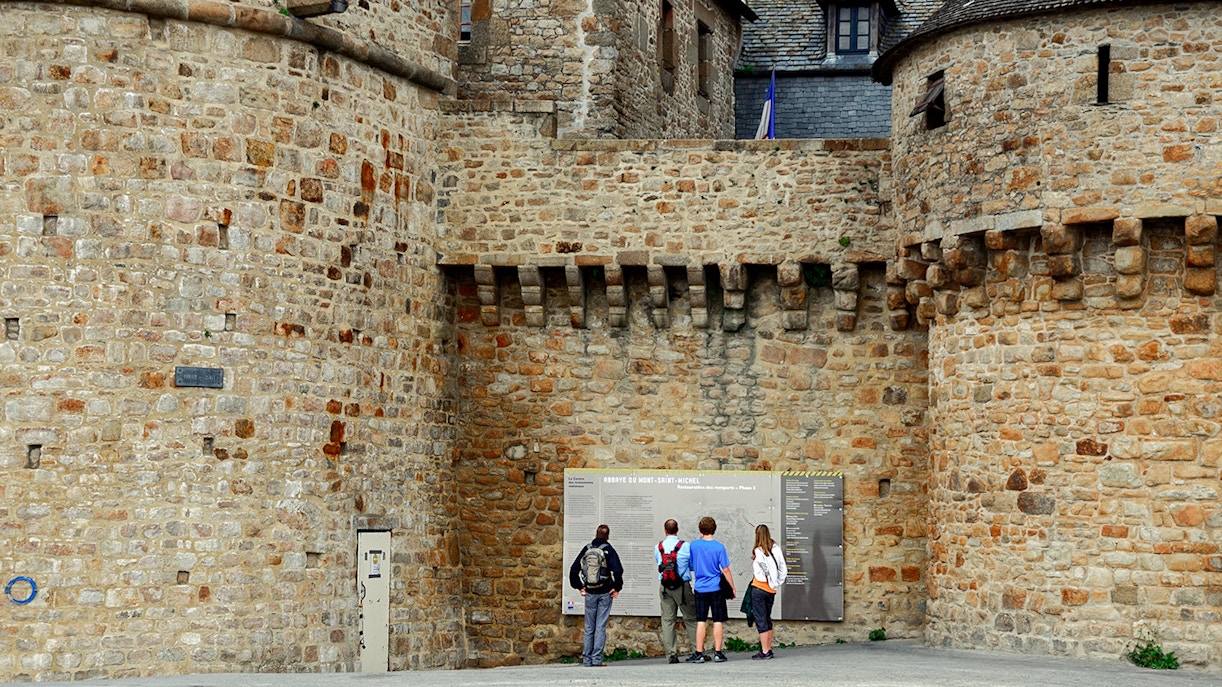 Visitors reading information on Mont Saint Michel's historic stone walls.