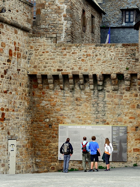 Visitors reading information on Mont Saint Michel's historic stone walls.