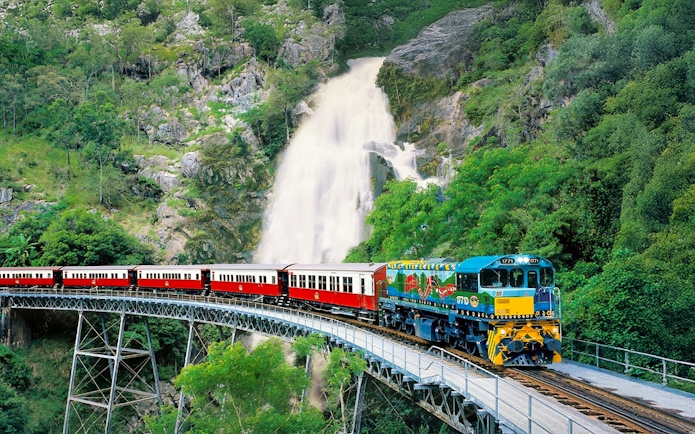 Kuranda Scenic Railway train crossing bridge with waterfall in background, Queensland, Australia.