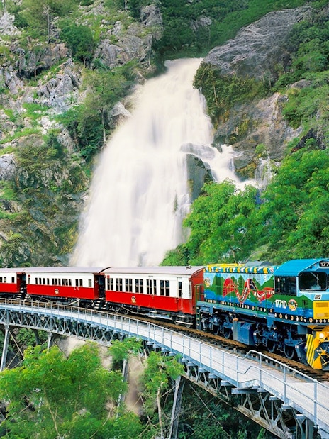 Kuranda Scenic Railway train crossing bridge with waterfall in background, Queensland, Australia.