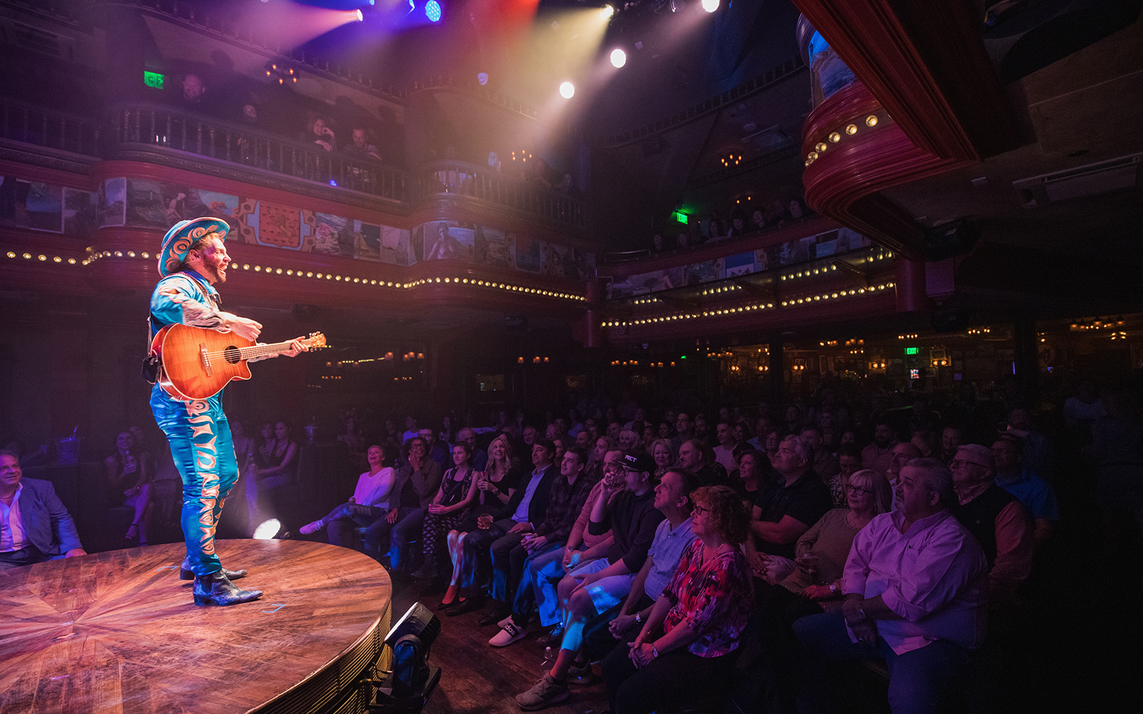 Performer with guitar on stage at Atomic Saloon Show, entertaining a lively audience.