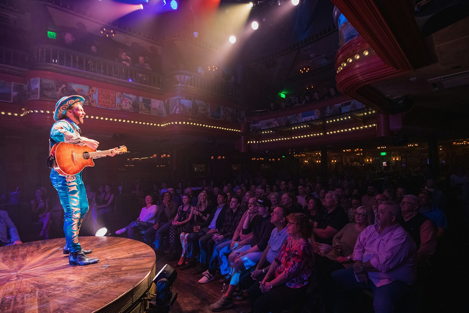 Performer with guitar on stage at Atomic Saloon Show, entertaining a lively audience.