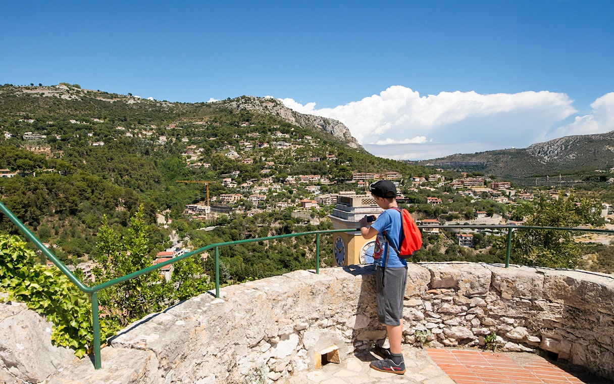 Child taking photo of Eze village landscape from a stone terrace, France.