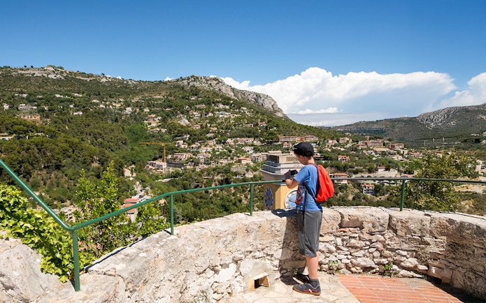 Child taking photo of Eze village landscape from a stone terrace, France.