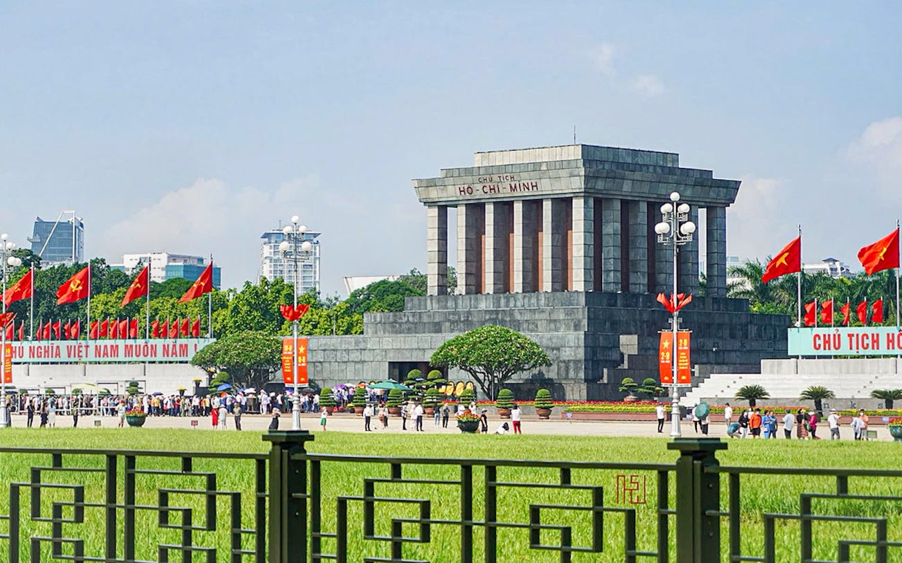 Ho Chi Minh Mausoleum in Hanoi with visitors and Vietnamese flags.