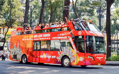 Hop-on Hop-off bus with tourists in Ho Chi Minh City, Vietnam, passing tree-lined street.