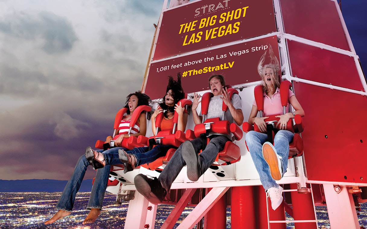 Riders on the Big Shot thrill ride at The Strat, Las Vegas, with city lights below.