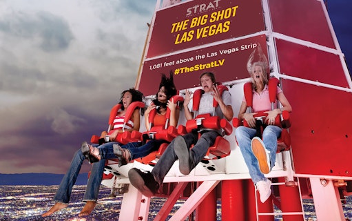 Riders on the Big Shot thrill ride at The Strat, Las Vegas, with city lights below.