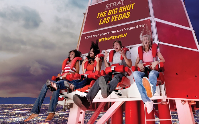 Riders on the Big Shot thrill ride at The Strat, Las Vegas, with city lights below.