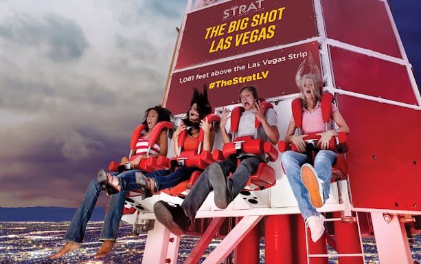 Riders on the Big Shot thrill ride at The Strat, Las Vegas, with city lights below.