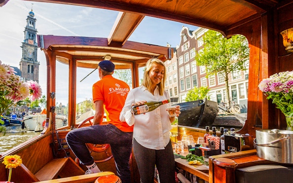 Guide serving wine on Amsterdam canal cruise boat with Westerkerk in background.