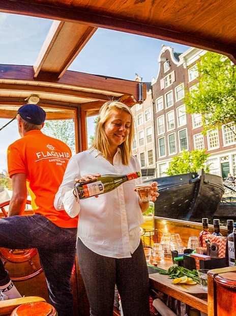 Guide serving wine on Amsterdam canal cruise boat with Westerkerk in background.