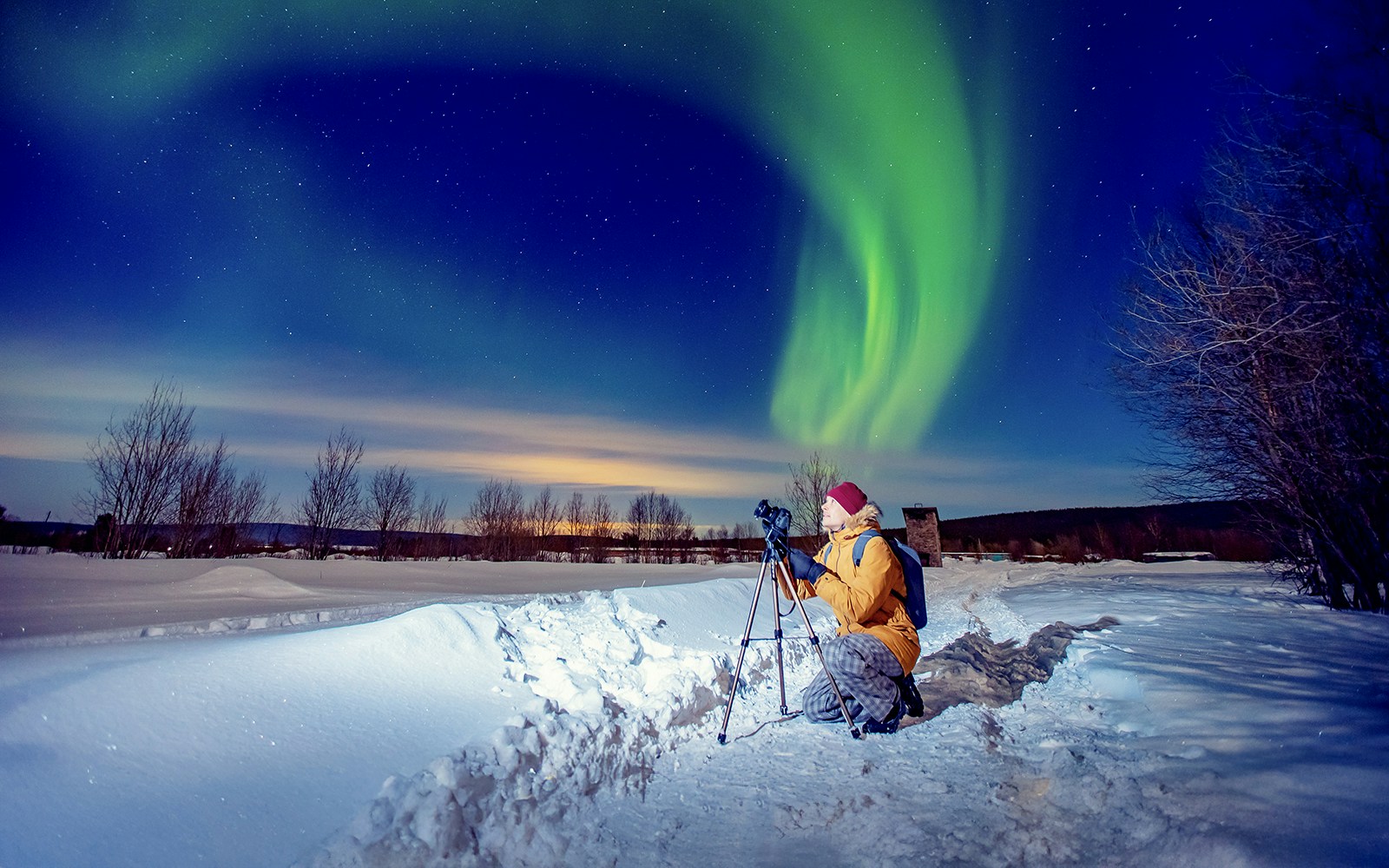Person photographing Northern Lights on snowy landscape during tour.