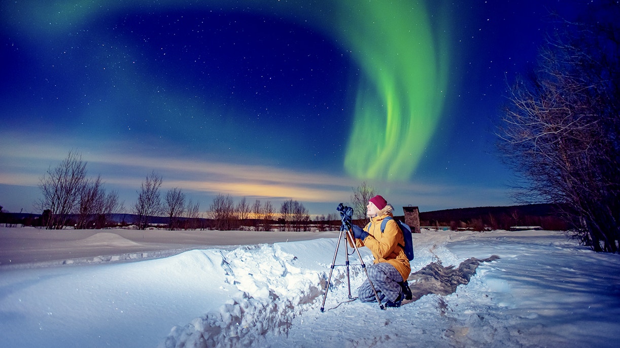 Person photographing Northern Lights on snowy landscape during tour.