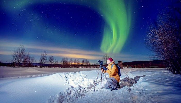 Person photographing Northern Lights on snowy landscape during tour.