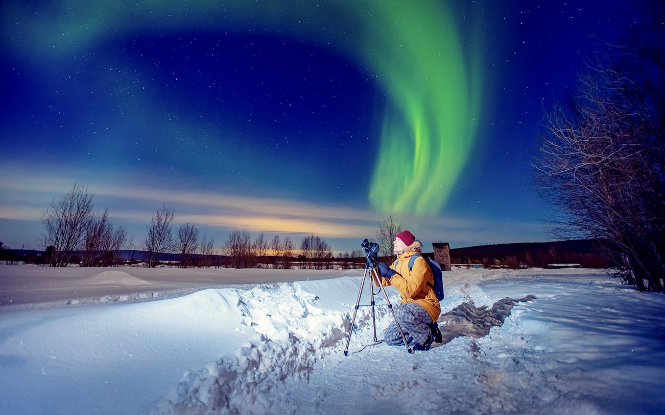 Person photographing Northern Lights on snowy landscape during tour.