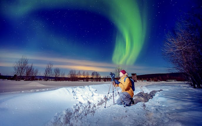 Person photographing Northern Lights on snowy landscape during tour.